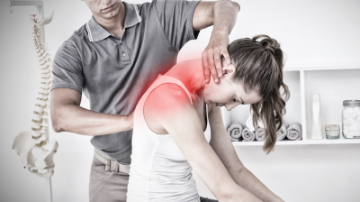 Therapeut wendet manuelle Therapie an der Schulter einer sitzenden Patientin an