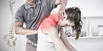 Therapeut wendet manuelle Therapie an der Schulter einer sitzenden Patientin an